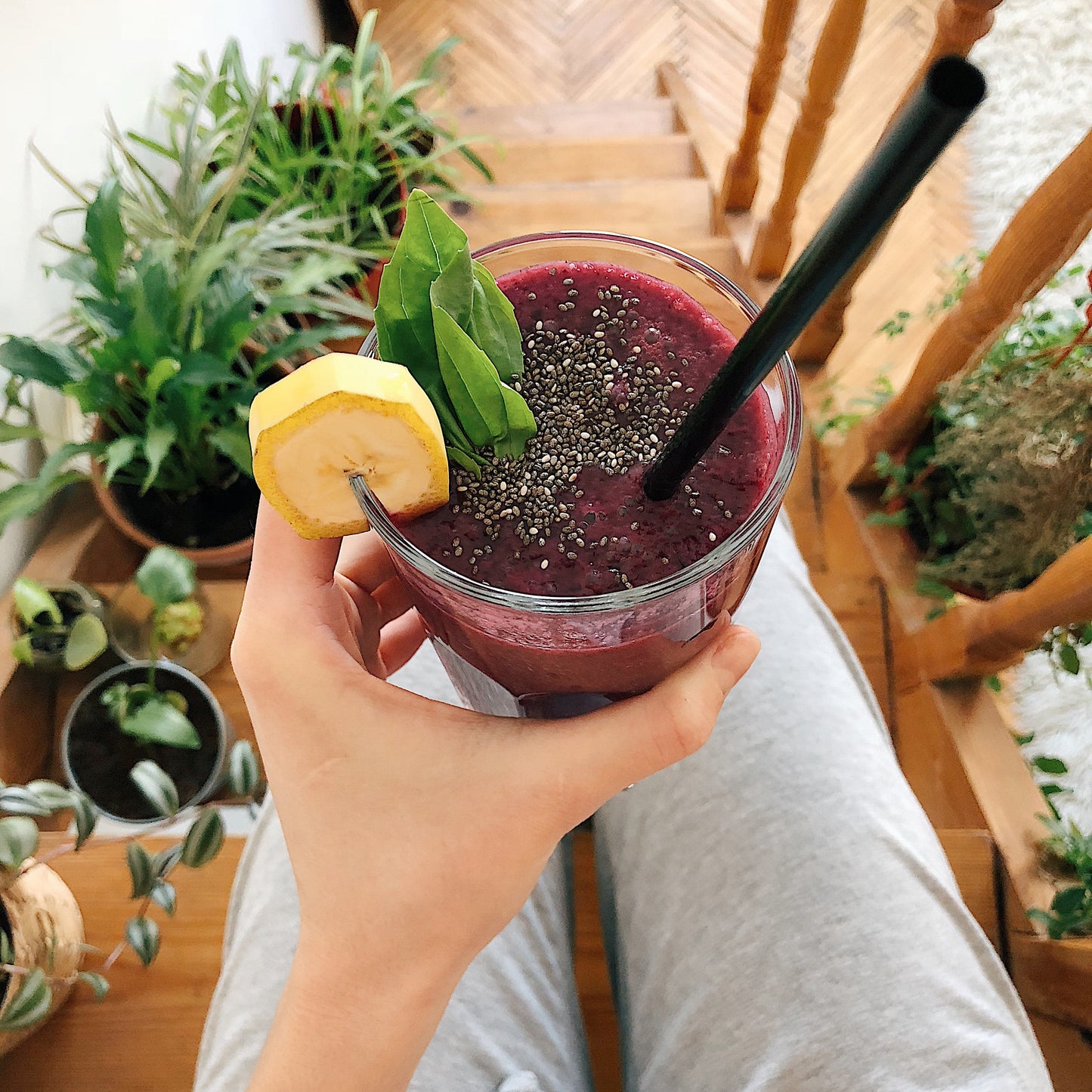 Smoothie glass held over someone's lap whilst sat on the stairs surrounded by plants